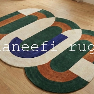 May include: Three oval rugs with geometric patterns. The rugs feature green, beige, brown, and blue sections. The text "haneefi rugs" is displayed across the rugs.