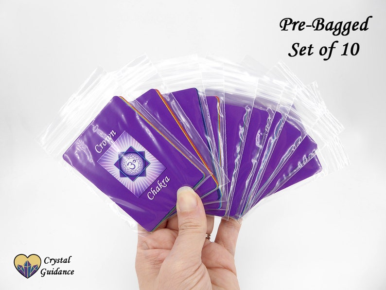Pu&ograve; includere: Un set di dieci carte dei chakra viola, ciascuna con un diverso simbolo e nome del chakra, sono pre-imballate in sacchetti di plastica trasparente individuali. Le carte sono etichettate con il nome e il simbolo del chakra. Il testo "Pre-Bagged Set of 10" &egrave; visibile nella parte superiore dell'immagine.
