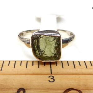 May include: A silver ring with a green gemstone. The ring is on a wooden ruler with the number 3 visible.