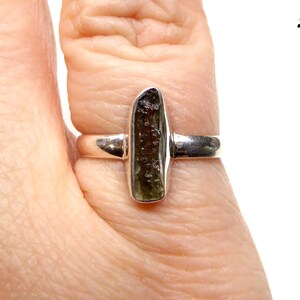 May include: A silver ring with a green and brown gemstone. The ring is on a finger.