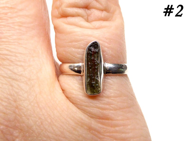 May include: A silver ring with a green and brown gemstone. The ring is on a finger.