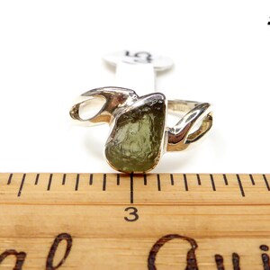 May include: A silver ring with a green gemstone set in a twisted band. The ring is shown next to a ruler, with the gemstone measuring approximately 1 inch in diameter.