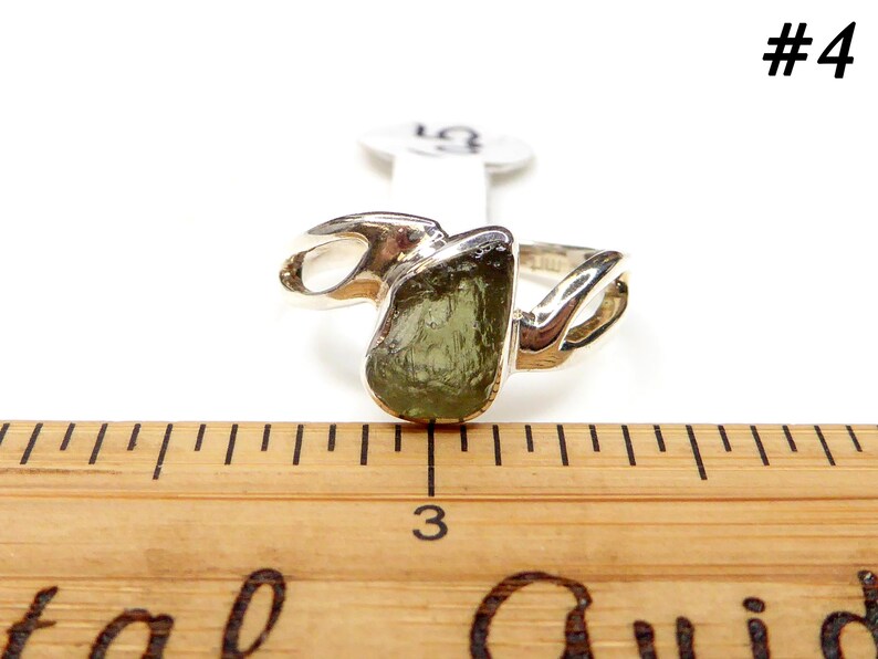 May include: A silver ring with a green gemstone set in a twisted band. The ring is shown next to a ruler, with the gemstone measuring approximately 1 inch in diameter.