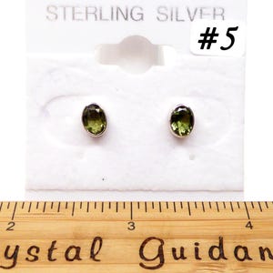 May include: A pair of sterling silver earrings with green oval-shaped gemstones. The earrings are displayed on a white card with the text "STERLING SILVER #5".