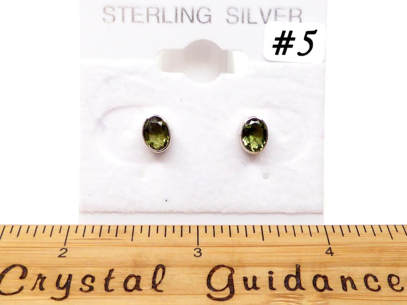 May include: A pair of sterling silver earrings with green oval-shaped gemstones. The earrings are displayed on a white card with the text "STERLING SILVER #5".