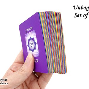 Pu&ograve; includere: Un set di 10 carte dei chakra viola con bordi arcobaleno. La carta superiore mostra il simbolo del chakra della corona e la parola "Corona" in testo bianco. Il testo "Unbagged Set of 10" &egrave; visibile nell'angolo in alto a destra dell'immagine.