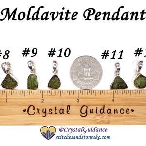 May include: Five silver pendants with green moldavite stones, numbered 8 through 12, are lined up on a wooden ruler with a "Crystal Guidance" logo. The ruler is marked in inches.