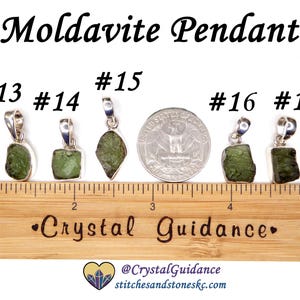 May include: Five silver pendants with green moldavite stones. The pendants are numbered 13, 14, 15, 16, and 17. The pendants are displayed on a wooden ruler with the text "Crystal Guidance" printed on it.