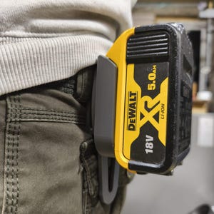 Peut inclure: Un bloc-batterie DeWalt 18V 5.0Ah Li-Ion noir et jaune fixé à un clip de ceinture gris. Le bloc-batterie est fixé au clip, qui est attaché à la ceinture d'une personne. Le bloc-batterie porte le logo DeWalt.