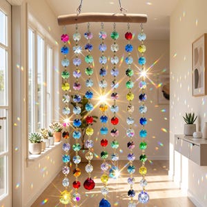 May include: A decorative crystal beaded curtain hangs from a wooden rod. The curtain features rows of colorful, faceted crystals in various colors, including red, blue, green, and yellow. The crystals are suspended by gold-colored chains, creating a shimmering effect.