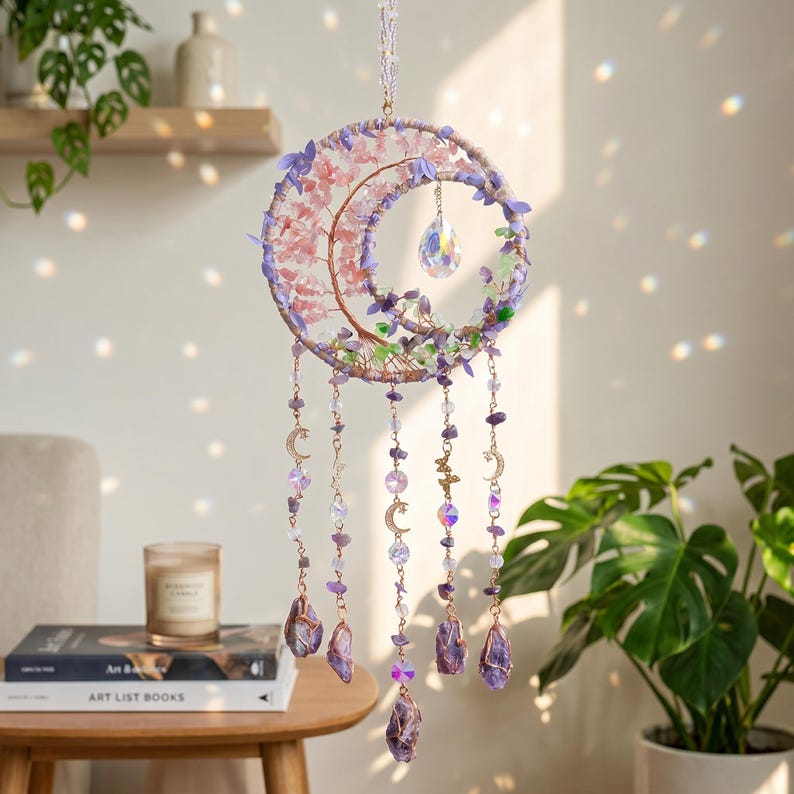 May include: A celestial-themed dream catcher with a crescent moon design. The dream catcher features a copper-colored wire frame adorned with pink and purple flowers, amethyst crystals, and hanging strands with moon and star charms.