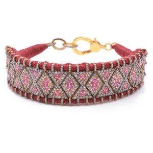 May include: A wide bracelet featuring a central band of dark red thread wrapped around a metal frame. The surface is decorated with a repeating geometric pattern of diamonds and triangles set with small pink stones and clear pavé crystals.