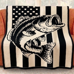 May include: A black and white throw blanket featuring a large fish design. The blanket has a striped pattern with a section resembling the American flag. The fish is detailed with open mouth and fins. The blanket is draped over an orange sofa.