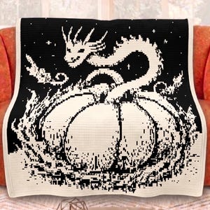 Puede incluir: Una manta de ganchillo negra y crema con un diseño de dragón y calabaza. El dragón es blanco, con un cuerpo largo y sinuoso. La calabaza es de color crema y el fondo es negro.