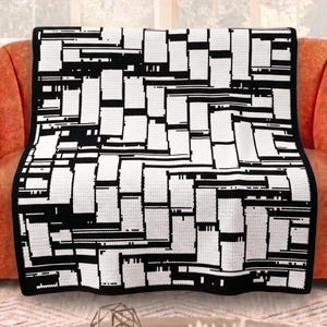 May include: A black and white crocheted blanket with a geometric pattern, draped over an orange sofa. The blanket features a repeating design of rectangular and linear shapes. The edges are finished with a solid black border.