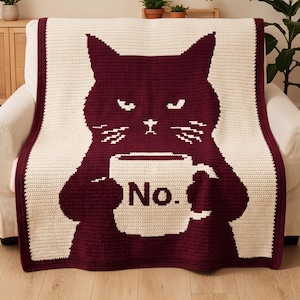 May include: A rectangular crochet blanket featuring a dark maroon cat silhouette against a cream background. The cat has a grumpy expression and holds a cream-colored mug with the word No. printed in dark maroon letters on the front surface.