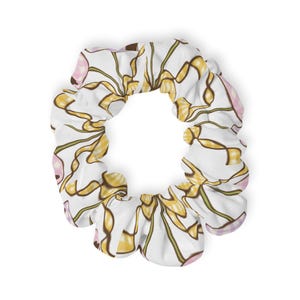 Può includere: Un elastico per capelli in tessuto bianco con un motivo ripetuto di forme astratte a nastro gialle e marroni, intervallate da piccole sezioni a quadretti rosa e bianchi. L'accessorio presenta una consistenza arricciata con interno elastico.