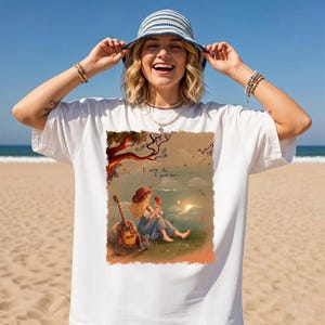 May include: A white short-sleeve t-shirt featuring a rectangular graphic print of a person sitting on grass with a guitar, a tree, and a sunset. The text "I knew it, I knew you..." is printed above the person. The shirt is worn with a blue and white striped bucket hat.