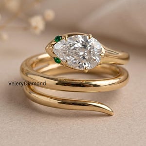 Può includere: Un anello in oro a forma di serpente con una pietra preziosa bianca taglio a pera come testa, accentuata da due piccole pietre verdi per gli occhi. La fascia ha un design a spirale e il testo VeleryDiamond è impresso sul lato dell'anello.