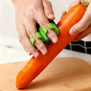 May include: A bright orange carrot being peeled with a green finger protector and peeler. The peeler has a black handle and is designed to protect fingers while preparing vegetables. The carrot rests on a wooden cutting board.