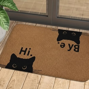 Puede incluir: Felpudo rectangular marrón con siluetas de gatos negros y las palabras "Hi." y "Bye." en negro. La alfombra está hecha de un material tejido y está colocada frente a una puerta.