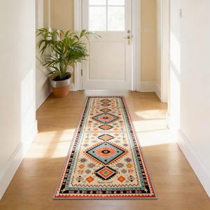 Könnte beinhalten: Ein langer, rechteckiger Teppich mit geometrischem Muster in einem Flur. Der Teppich hat einen cremefarbenen Hintergrund mit rautenförmigen Mustern in Türkis, Orange, Schwarz und Rot. Der Teppich ist etwa 244 cm lang.