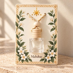 Peut inclure: Un petit flacon en verre transparent avec un bouchon en bois clair est suspendu par une cordelette tressée sur une carte rectangulaire. La carte présente un emblème solaire doré, des fleurs de jasmin blanches et le texte Mabuhay.