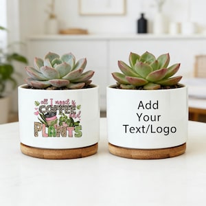 May include: Two white ceramic planters with succulents. One planter has the text "all I need is coffee and plants" with a coffee cup and plant graphic. The other planter has the text "Add Your Text/Logo". Both planters sit on a wooden base.