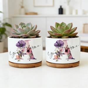 May include: Two white ceramic planters with succulents. Each planter features a large floral letter "A" with the words "Your Name" in script. The planters sit on bamboo saucers.