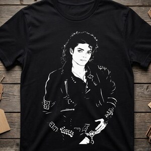 May include: A black short-sleeved t-shirt featuring a high-contrast white graphic print of a person with curly hair wearing a leather jacket adorned with multiple buckles, zippers, and metallic hardware details across the chest and sleeves.