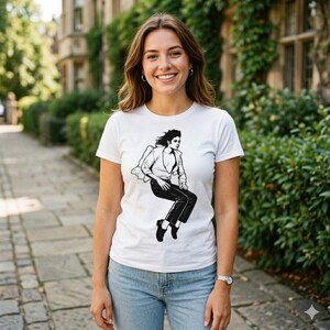 May include: A white short-sleeved t-shirt featuring a black graphic illustration of a person with dark hair wearing a button-down shirt and dark trousers, captured in a dynamic pose with one leg bent while appearing to leap or dance.