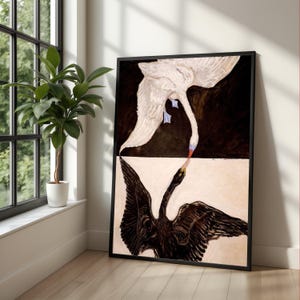 May include: A framed art print featuring a white swan above a black swan, with their beaks nearly touching. The artwork has a black background above a cream-colored section. The swans are painted with detailed brushstrokes, creating a striking contrast.