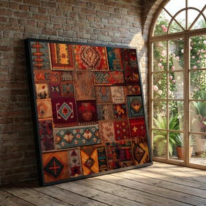 May include: A framed, colorful patchwork rug with a black frame leans against a brick wall. The rug features a variety of geometric patterns in shades of red, blue, yellow, and brown. A large arched window with a garden view is in the background.