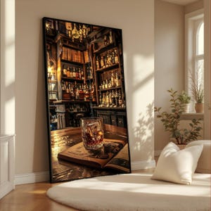 May include: A framed print depicting a bar interior. A tumbler of whiskey with ice rests on an open book on a wooden table. The bar is stocked with bottles and shelves, illuminated by warm lighting. A white cushion and rug are in the foreground.