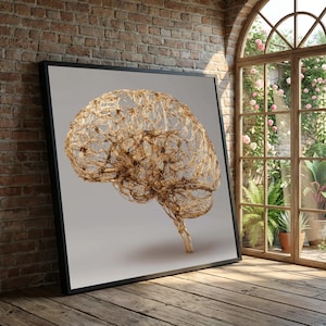 Op de afbeelding: Een ingelijst kunstwerk met een gedetailleerde, gouden draadsculptuur van een menselijk brein. Het brein staat tegen een lichtgrijze achtergrond, met een zwart frame. Het kunstwerk wordt tentoongesteld op een houten vloer, nabij een bakstenen muur en een raam.