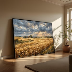 May include: A framed landscape painting depicts a golden wheat field under a dramatic sky with sun rays breaking through the clouds. A dirt road leads to a small village in the distance. The artwork is displayed on a wooden floor.