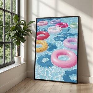 Könnte beinhalten: Ein gerahmter Wandkunstdruck, der ein Schwimmbecken mit mehreren bunten aufblasbaren Schwimmringen zeigt. Die kreisförmigen Ringe in Rosa, Gelb, Lila, Grün und Weiß mit Streuseln schwimmen auf dem klaren, blauen und leicht gewellten Wasser.