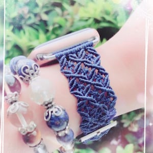Pode incluir: Uma pulseira de relógio em macramé azul-escuro com um padrão de nós complexo ligado a um conector metálico, combinada com uma pulseira de contas com pedras redondas azuis, roxas e transparentes separadas por espaçadores de metal prateado.