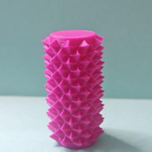 May include: A bright pink, cylindrical object with a textured, spiky surface. The object has a flat top and bottom, and the spiky pattern covers the entire body. The background is a light blue.