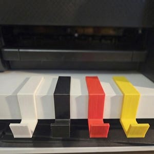 May include: A printer with four coloured paper guides: white, black, red, and yellow. The guides are attached to a stack of white paper, and the printer is in the background.