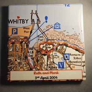 Może przedstawiać: Kwadratowa ceramiczna podstawka z mapą Whitby, z punktami orientacyjnymi oraz imionami "Ruth and Mark" i "3rd April 2004". Podstawka ma błyszczące wykończenie i szczegółowy wzór mapy.