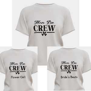 May include: Three light gray short-sleeved t-shirts with black text. The top shirt reads "Hen Do CREW" with heart icons. The bottom left shirt adds "Flower Girl" and the bottom right shirt adds "Bride's Bestie" below the same graphic design.