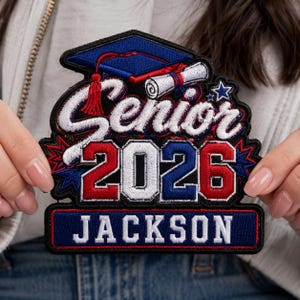 Op de afbeelding: Geborduurde patch met de tekst "Senior 2026 JACKSON". De patch heeft een afstudeerhoed, diploma en sterren in rood, wit en blauw. De patch is rechthoekig met een zwarte rand.