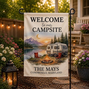 May include: A beige garden flag with a camping scene, featuring a camper, campfire, and chairs near a lake and mountains. The flag reads "WELCOME to our CAMPSITE" and "THE MAYS CONOWINGO, MARYLAND."