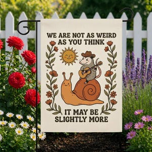 Może przedstawiać: Kremowa flaga ogrodowa z napisem "WE ARE NOT AS WEIRD AS YOU THINK IT MAY BE SLIGHTLY MORE." Flaga przedstawia kreskówkową ilustrację ślimaka, oposa grającego na gitarze i uśmiechniętego słońca.