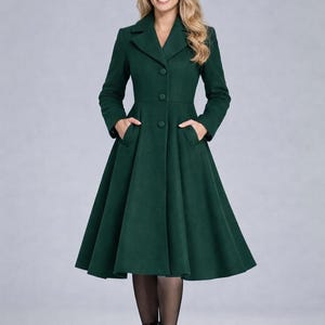 May include: A long, emerald green coat with a flared skirt and a classic button-down design. The coat features a notched collar, long sleeves, and pockets. The model is wearing black boots and pantyhose.