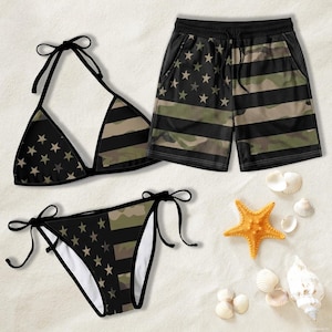 Könnte beinhalten: Ein schwarzes und camouflagefarbenes Bikini-Set und passende Shorts mit Stern- und Streifenmuster. Das Bikini-Oberteil und -Unterteil haben schwarze Bindebänder. Die Shorts haben einen schwarzen Mesh-Überzug. Das Set wird auf einer sandigen Oberfläche mit Muscheln und einem Seestern präsentiert.