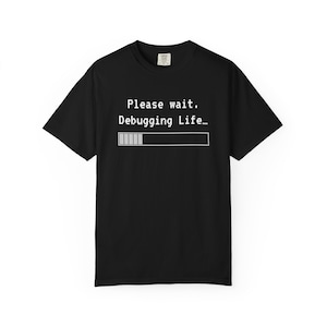 May include: Black t-shirt with the text "Please wait. Debugging Life..." in white, along with a loading bar graphic. The shirt has short sleeves and a crew neck.