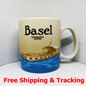 Könnte beinhalten: Cremefarbene Keramiktasse mit dem schwarzen Wort "Basel" und darunter "Starbucks Coffee". Auf der Tasse befindet sich eine Bootsillustration mit blauem Wasser am Boden. Die Tasse hat einen gebogenen Griff.