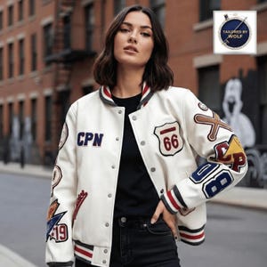 Może przedstawiać: Kremowa kurtka typu varsity z naszywkami, w tym "CPN" i "66". Kurtka ma zapinany na guziki przód, paski na kołnierzu, mankietach i obszyciu. Naszywki mają różne kolory i wzory, tworząc sportową estetykę.